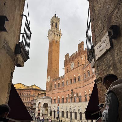 View of Torre del Mangia and Palazzo Pubblico through a narrow alley in Siena, a picturesque stop on a Siena day trip from Florence