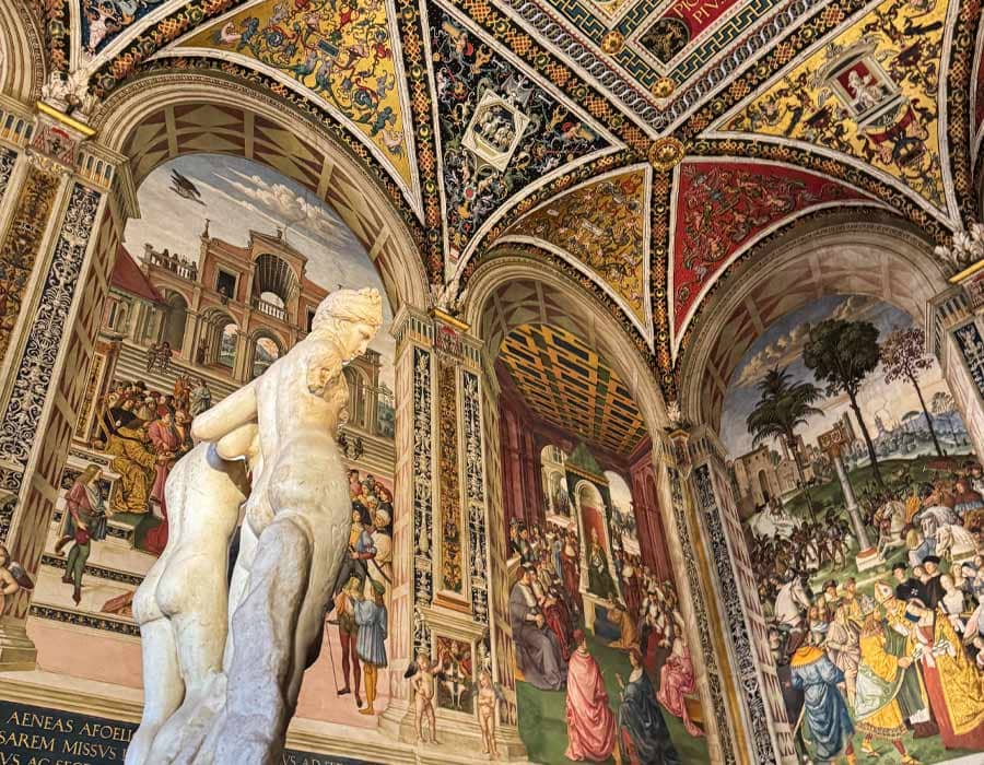 Intricate frescoes and marble statue inside Siena Cathedral's Piccolomini Library, a cultural treasure to explore on a Siena day trip from Florence.