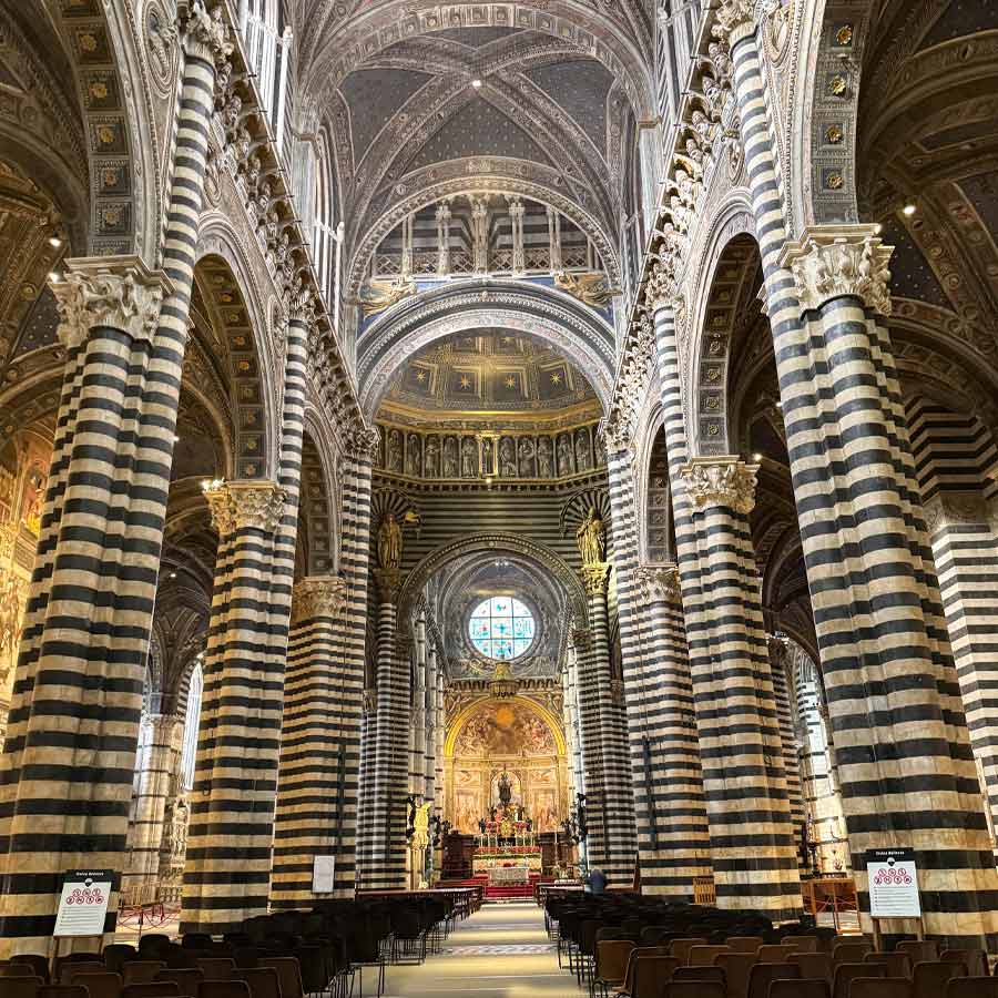 Interior nave of Siena Cathedral with striped black-and-white marble columns and ornate vaulted ceilings
