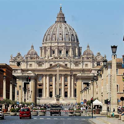 Front view of St. Peter’s Basilica in Vatican City, with tourists and traffic on Via della Conciliazione.