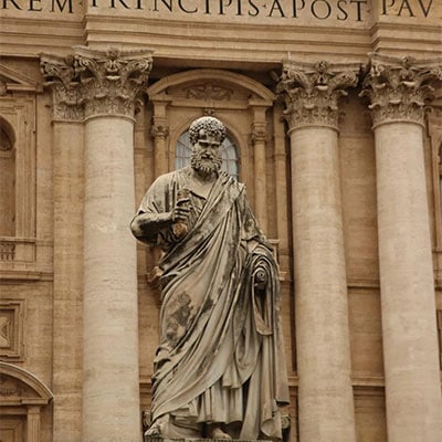 Marble statue of Saint Peter holding keys and a scroll, in front of the façade of St. Peter’s Basilica in Vatican City.