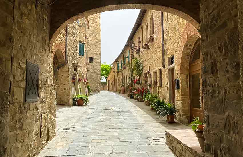 Stone-paved street with flowers and medieval arches in San Donato in Poggio, Tuscany, Italy