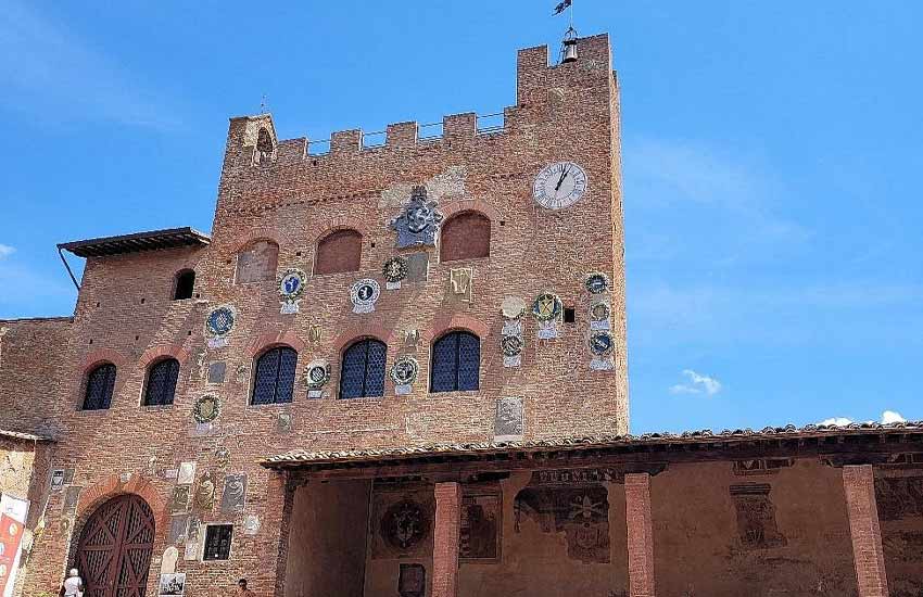 Palazzo Pretorio in Certaldo with medieval coats of arms and clock tower under a blue sky