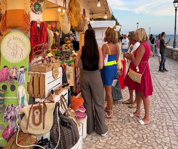 People shopping at a Sperlonga night market stall selling handmade bags, hats, and local crafts by the seaside.