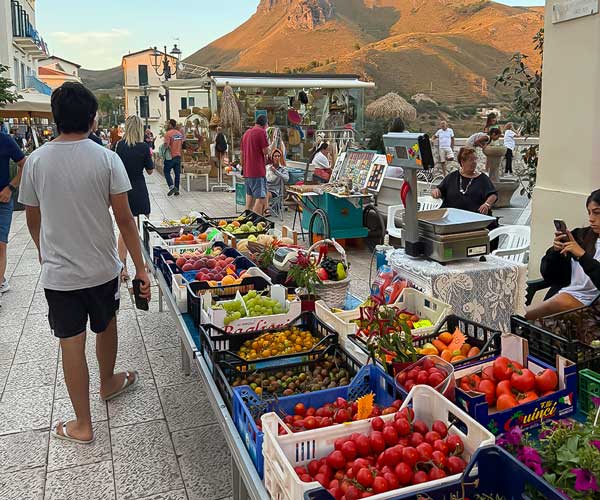 Fresh fruits and vegetables on display at Sperlonga’s outdoor market with people shopping in the evening.