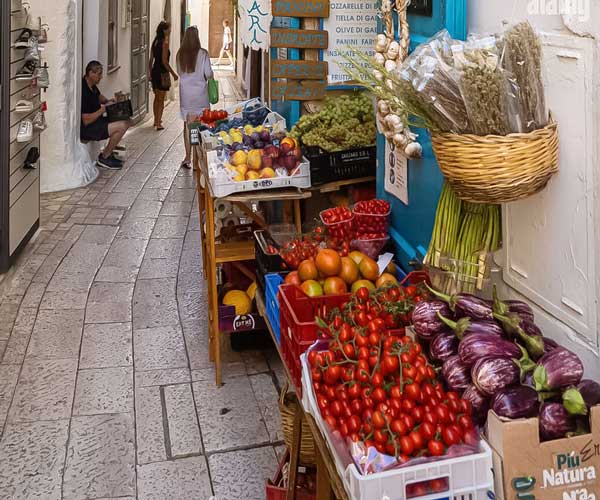 Fresh fruits and vegetables on display at Sperlonga’s outdoor market with people shopping in the evening.